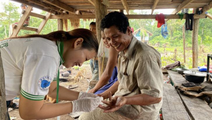 Mobile malaria worker Sum (left) takes a blood sample from Peng (right) to test for malaria, October 2022. Sum makes an eight-day trip every month to remote areas of Ratanakiri Province to provide malaria services to families like Peng’s. Photo: Malaria Consortium