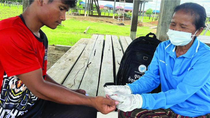 Ms Chan Phum, a village malaria worker, Keng Ngey Village, Stung Treng Province, performs a malaria blood test for a worker who recently returned from the forest. Ms Chan Phum believes that PSEAH is doable if the health providers are well aware of the principles, mindful of their behaviour, and are role models for the community members. Photo by Linna Khorn/CRS